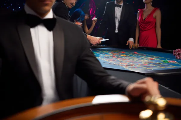 A professional dealer in a tuxedo greeting players at the roulette table, symbolizing the authentic live casino feel at ZEUS75.